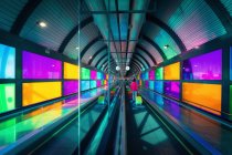 Unrecognizable woman with suitcase riding mowing walkway near colorful panels inside Madrid Barajas Airport in Spain — Stock Photo