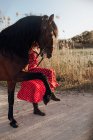 Femme en robe rouge tachetée menant cheval de prairie sur le chemin près de prairie — Photo de stock