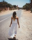 Vista trasera de la mujer con vestido de verano blanco mientras camina por la calle del desierto de la ciudad marroquí - foto de stock