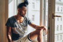 Вдумливий афроамериканець людина з косами сидячи вдома на підвіконня — стокове фото