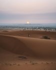 Rückansicht einer barfüßigen Frau im Sommerkleid, die auf einer Sanddüne in der endlosen Wüste im Sonnenuntergang spaziert, Marokko — Stockfoto
