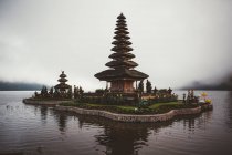 Pequeño complejo de pagoda de oración con jardín verde alrededor construido en agua en la orilla contra la niebla, Bali - foto de stock