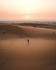 Back view of barefoot man in summer shirt walking on sandy dune of endless desert in sunset, Morocco — Stock Photo