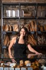 Mulher bonita em avental preto vendendo baguete francês na padaria — Fotografia de Stock