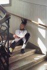 Красивый афроамериканец с плетеными волосами сидит на лестнице и смотрит на руки — стоковое фото