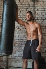 Уверенный чернокожий боксер в спортзале позирует с боксерской сумкой — стоковое фото