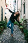 Giovane bruna casual in occhiali in piedi in posa aggraziata mentre balla sulla strada di ciottoli della città vecchia — Foto stock