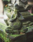 Stone fence with statue of praying monk covered with moss — Stock Photo