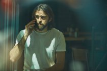 Молодий бородатий красивий чоловік у кафе за вікном розмовляє по телефону — стокове фото