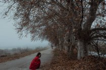 Mulher sonhadora em vestido vermelho na estrada vazia de terreno misterioso ensombrado — Fotografia de Stock