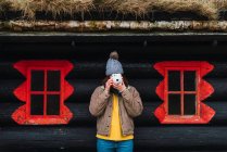 Жінка в зимовому одязі перед дерев'яною кабіною фотографує — стокове фото