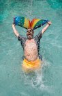 Веселый мужчина в купальниках кричит и машет флагом ЛГБТ, плескаясь в бассейне на курорте — стоковое фото