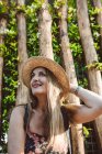 Задоволення дорослої жінки в літньому капелюсі соломи, посміхаючись на вулиці проти зелених дерев — стокове фото
