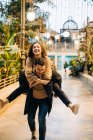 Excited young male giving piggyback ride to cheerful young female while walking along path during romantic date on city street — Stock Photo