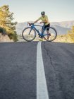 Здоровий чоловік відпочиває стоячи з велосипедом на гірській дорозі в сонячний день — стокове фото