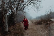 Mulher sonhadora em vestido vermelho andando ao longo da estrada vazia de terreno misterioso hazed — Fotografia de Stock