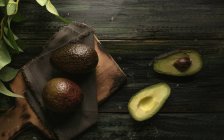 Свіжі цілі та наполовину авокадо на дерев'яному столі — стокове фото
