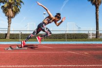 Atleta feminina forte em sportswear correndo rápido contra o céu azul no dia ensolarado no estádio — Fotografia de Stock