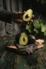 Menschenhand hält halbierte Avocado über Holztisch — Stockfoto