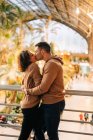 Веселые юноша и девушка обнимаются и целуются, стоя внутри освещенного павильона во время свидания — стоковое фото