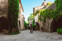 Back view of unrecognizable woman in dress and hat outstretching arms, on street of a medieval town — Stock Photo