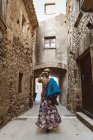 Вид ззаду на невпізнавану жінку в сукні і капелюсі, що йде по вулиці середньовічного міста — стокове фото