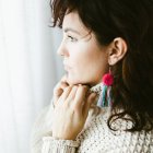 Side view of attractive dreamy young brunette with bright handmade earring of colorful threads — Stock Photo