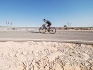 Healthy man riding bicycle on road in sunny day with barren landscape on background — Stock Photo