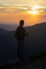 Silueta de vista trasera de un hombre mayor con mochila y bastón de madera senderismo contemplando increíble paisaje de montaña - foto de stock