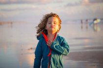 Lockiges Kind in gestreiften Spaziergängen am Strand auf verschwommenem Naturhintergrund — Stockfoto