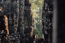Antiguo monumento de piedra con esculturas de cara en la pared iluminada con la luz del sol, Tailandia - foto de stock