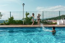 Freunde spielen an einem sonnigen Sommertag mit Wasserpistolen im Pool — Stockfoto