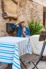 Woman in straw hat and dress sitting on terrace of restaurant in medieval town — Stock Photo