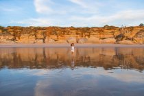 Bambino riccio che cammina sull'acqua sulla spiaggia di sabbia sullo sfondo della natura offuscata — Foto stock