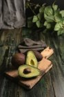 Avocats frais entiers et coupés en deux sur table rustique en bois — Photo de stock