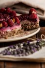 Нарізаний соковитий фруктовий торт з малиною на білій тарілці на дерев'яному столі, прикрашеному лавандовим букетом — стокове фото