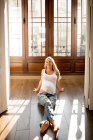 Glückliche schwangere Frau lächelt und schaut weg, während sie an sonnigen Tagen auf dem Boden in einem geräumigen Zimmer sitzt — Stockfoto