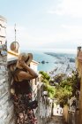 Неузнаваемая женщина в летнем наряде стоит на каменной лестнице и смотрит на побережье моря — стоковое фото