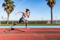 Starke Athletin in Sportbekleidung läuft an sonnigem Tag im Stadion gegen blauen Himmel an — Stockfoto