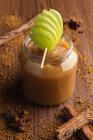 Decorated with green apple appetizing juicy applesauce in glass jar and cinnamon on wooden background — Stock Photo