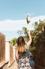 Excited unrecognizable woman tossing straw hat up on narrow street in sunshine — Stock Photo