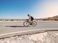Здоровий чоловік їде на велосипеді по дорозі в сонячний день з безплідним пейзажем на фоні — стокове фото