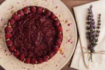 Нарізаний соковитий фруктовий торт з малиною на білій тарілці на дерев'яному столі, прикрашеному лавандовим букетом — стокове фото