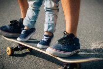 Сверху ноги в кроссовках ребенка и родителя стоят на скейтборде на дороге в солнечный день — стоковое фото