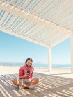 Hombre barbudo navegando teléfono inteligente mientras está sentado en gazebo en la playa de arena cerca del mar en el día soleado - foto de stock