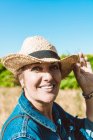Smiling mature woman in hat looking at camera in sunny field — Stock Photo