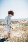 Вид сбоку симпатичного ребенка, стоящего босыми ногами в песке на красивом пляже в солнечный день — стоковое фото