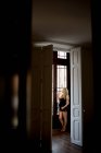 Femme enceinte réfléchie en lingerie debout près de la porte ouverte à la maison — Photo de stock