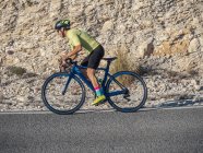 Крупный план здорового человека, катающегося на велосипеде по горной дороге в солнечный день — стоковое фото