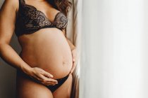 Closeup of pregnant woman in underwear standing at home and holding belly — Stock Photo